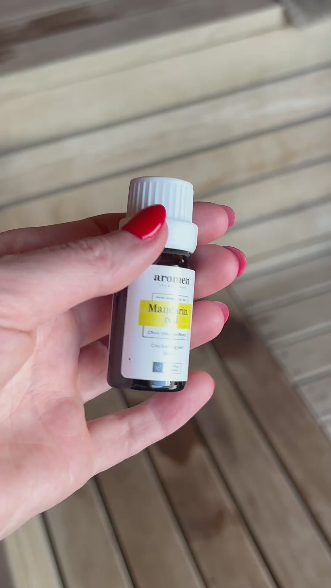 Rød mandarin eterisk olje fra Aromen holdt i hånd i badstumiljø